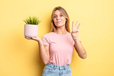Güzel sarışın kız gülümsüyor ve arkadaş canlısı görünüyor, üç numarayı gösteriyor. ev bitkisi kavramı