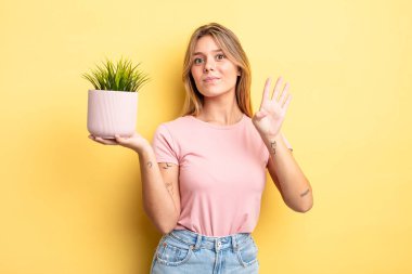 Güzel sarışın kız gülümsüyor ve arkadaş canlısı görünüyor, dört numarayı gösteriyor. ev bitkisi kavramı