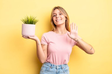 Güzel sarışın kız mutlu bir şekilde gülümsüyor, el sallıyor, hoş geldin diyor ve seni selamlıyor. ev bitkisi kavramı