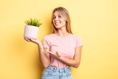 Güzel sarışın kız neşeyle gülümsüyor, mutlu hissediyor ve bir konsept gösteriyor. ev bitkisi kavramı