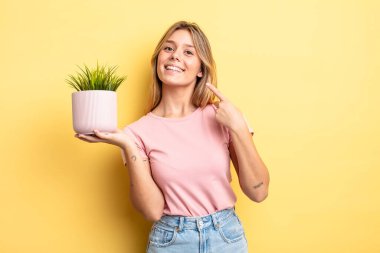 Güzel sarışın kız kendi gülüşünü göstererek kendine güvenerek gülümsüyor. ev bitkisi kavramı