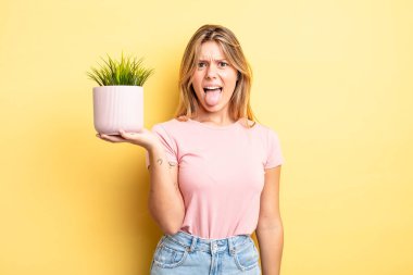 Güzel sarışın kız iğreniyor, sinirleniyor ve dilini çıkarıyor. ev bitkisi kavramı