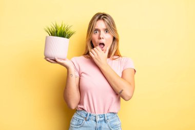 Güzel sarışın kız, ağzı ve gözleri sonuna kadar açık ve eli çenesinde. ev bitkisi kavramı