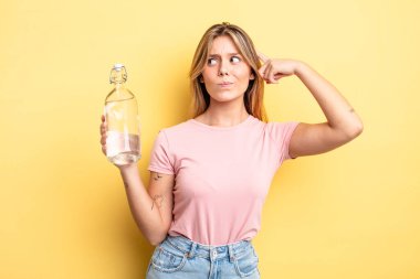 Güzel sarışın kız şaşkın ve kafası karışık, kaşınan bir kafa hissediyor. su şişesi kavramı