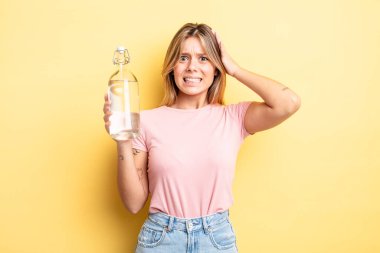 Güzel sarışın kız stresli, endişeli ya da korkmuş, elleri başının üstünde. su şişesi kavramı