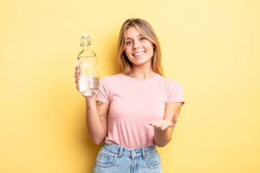 Güzel sarışın kız mutlu bir şekilde gülümsüyor ve bir konsept sunuyor. su şişesi kavramı