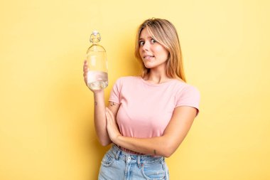 Güzel sarışın kız omuz silkiyor, kafası karışık ve kararsız. su şişesi kavramı