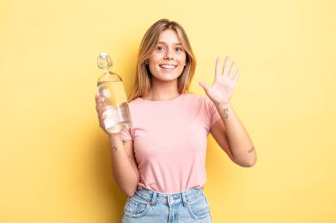 Güzel sarışın kız gülümsüyor ve arkadaş canlısı görünüyor, beş numarayı gösteriyor. su şişesi kavramı