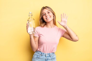 Güzel sarışın kız mutlu bir şekilde gülümsüyor, el sallıyor, hoş geldin diyor ve seni selamlıyor. su şişesi kavramı