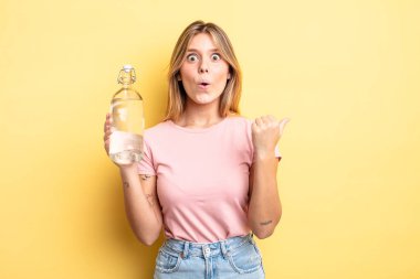 Güzel sarışın kız inançsızlıktan şaşkın şaşkın bakıyor. su şişesi kavramı