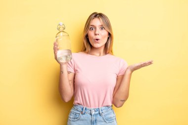 Güzel sarışın kız şaşırmış ve şok olmuş görünüyor. Çenesi düşmüş ve elinde bir nesne var. su şişesi kavramı