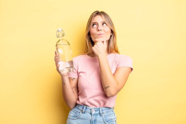 Güzel sarışın kız düşünüyor, kuşkulu ve şaşkın hissediyor. su şişesi kavramı