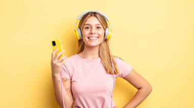 Güzel sarışın kız mutlu bir şekilde gülümsüyor, eli kalçasında ve kendinden emin. müzik konseptini dinlemek