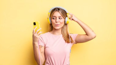 Güzel sarışın kız şaşkın ve kafası karışık, kaşınan bir kafa hissediyor. müzik konseptini dinlemek