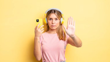 Güzel sarışın kız ciddi görünüyor. Avuç içini gösteriyor. Durma hareketi yapıyor. müzik konseptini dinlemek