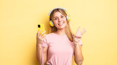 Güzel sarışın kız gülümsüyor ve arkadaş canlısı görünüyor, üç numarayı gösteriyor. müzik konseptini dinlemek