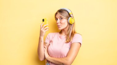 Güzel sarışın kız omuz silkiyor, kafası karışık ve kararsız. müzik konseptini dinlemek