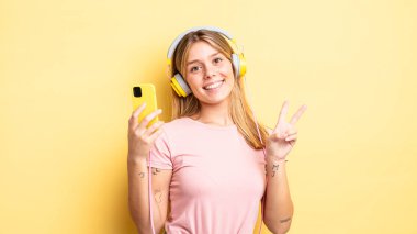 Güzel sarışın kız gülümsüyor ve arkadaş canlısı görünüyor. İki numarayı gösteriyor. müzik konseptini dinlemek