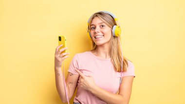 Güzel sarışın kız neşeyle gülümsüyor, mutlu hissediyor ve bir tarafı işaret ediyor. müzik konseptini dinlemek