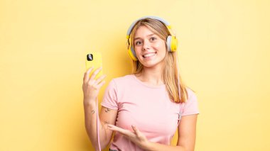 Güzel sarışın kız neşeyle gülümsüyor, mutlu hissediyor ve bir konsept gösteriyor. müzik konseptini dinlemek