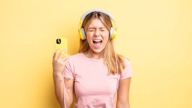 Güzel sarışın kız agresif bir şekilde bağırıyor, çok kızgın görünüyor. müzik konseptini dinlemek