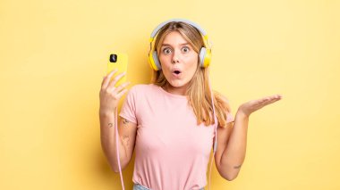 Güzel sarışın kız şaşırmış ve şok olmuş görünüyor. Çenesi düşmüş ve elinde bir nesne var. müzik konseptini dinlemek