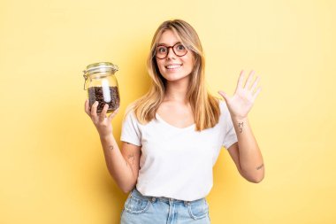 Güzel sarışın kız gülümsüyor ve arkadaş canlısı görünüyor, beş numarayı gösteriyor. kahve çekirdeği konsepti