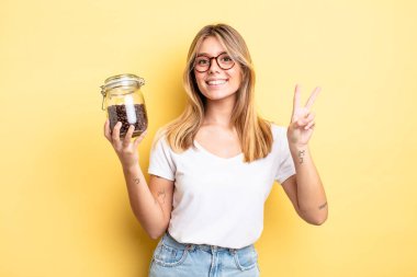 Güzel sarışın kız gülümsüyor ve arkadaş canlısı görünüyor. İki numarayı gösteriyor. kahve çekirdeği konsepti