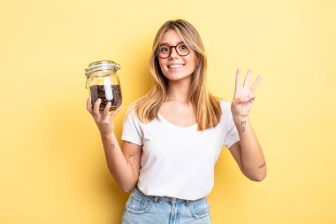 Güzel sarışın kız gülümsüyor ve arkadaş canlısı görünüyor, üç numarayı gösteriyor. kahve çekirdeği konsepti