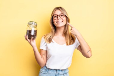 Güzel sarışın kız kendi gülüşünü göstererek kendine güvenerek gülümsüyor. kahve çekirdeği konsepti