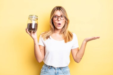 Güzel sarışın kız şaşırmış ve şok olmuş görünüyor. Çenesi düşmüş ve elinde bir nesne var. kahve çekirdeği konsepti