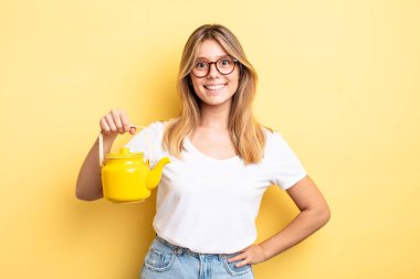 Güzel sarışın kız mutlu bir şekilde gülümsüyor, eli kalçasında ve kendinden emin. çaydanlık konsepti