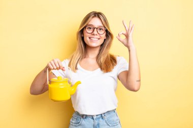 Güzel sarışın kız kendini mutlu hissediyor, iyi bir jestle onaylıyor. çaydanlık konsepti