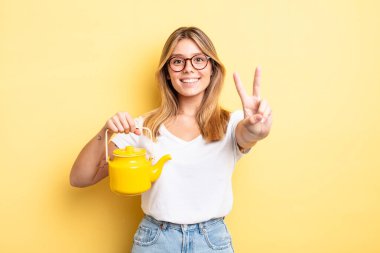 Güzel sarışın kız gülümsüyor ve mutlu görünüyor, zafer ya da barış işareti yapıyor. çaydanlık konsepti