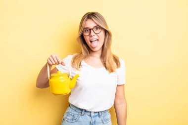 Güzel sarışın, neşeli ve asi tavırlı, şaka yapan ve dilini dışarı çıkaran bir kız. çaydanlık konsepti