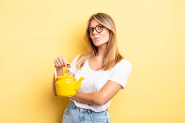 Güzel sarışın kız omuz silkiyor, kafası karışık ve kararsız. çaydanlık konsepti