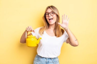 Güzel sarışın kız mutlu bir şekilde gülümsüyor, el sallıyor, hoş geldin diyor ve seni selamlıyor. çaydanlık konsepti