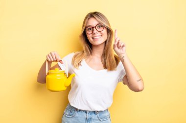 Güzel sarışın kız gülümsüyor ve arkadaş canlısı görünüyor. Bir numarayı gösteriyor. çaydanlık konsepti