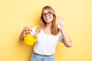 Güzel sarışın kız gülümsüyor ve arkadaş canlısı görünüyor, dört numarayı gösteriyor. çaydanlık konsepti