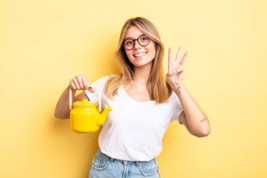 Güzel sarışın kız gülümsüyor ve arkadaş canlısı görünüyor, üç numarayı gösteriyor. çaydanlık konsepti