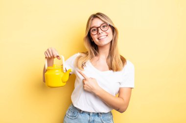 Güzel sarışın kız neşeyle gülümsüyor, mutlu hissediyor ve bir tarafı işaret ediyor. çaydanlık konsepti