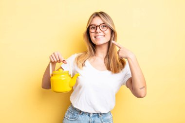 Güzel sarışın kız kendi gülüşünü göstererek kendine güvenerek gülümsüyor. çaydanlık konsepti