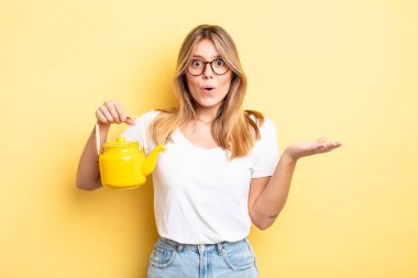 Güzel sarışın kız şaşırmış ve şok olmuş görünüyor. Çenesi düşmüş ve elinde bir nesne var. çaydanlık konsepti