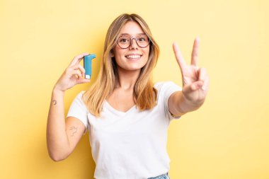 Güzel sarışın kız gülümsüyor ve mutlu görünüyor, zafer ya da barış işareti yapıyor. astım spreyi kavramı