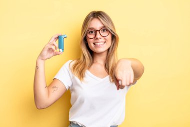 Güzel sarışın kız seni seçen kamerayı işaret ediyor. astım spreyi kavramı