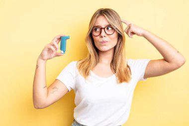 Güzel sarışın kız mutlu bir şekilde gülümsüyor ve hayal kuruyor ya da şüphe ediyor. astım spreyi kavramı