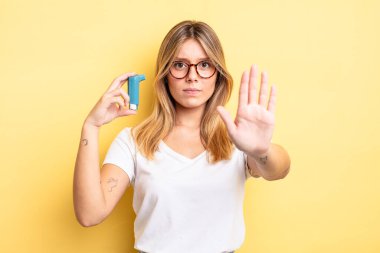 Güzel sarışın kız ciddi görünüyor. Avuç içini gösteriyor. Durma hareketi yapıyor. astım spreyi kavramı