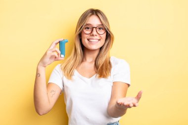 Güzel sarışın kız mutlu bir şekilde gülümsüyor ve bir konsept sunuyor. astım spreyi kavramı