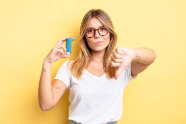 Güzel sarışın kız kendini kötü hissediyor, baş parmağını kaldırıyor. astım spreyi kavramı