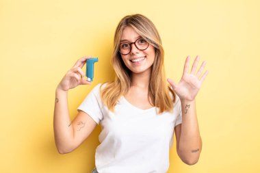 Güzel sarışın kız gülümsüyor ve arkadaş canlısı görünüyor, beş numarayı gösteriyor. astım spreyi kavramı